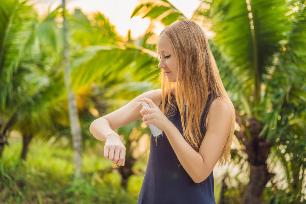 Woman spraying insect repellent on skin outdoor.
